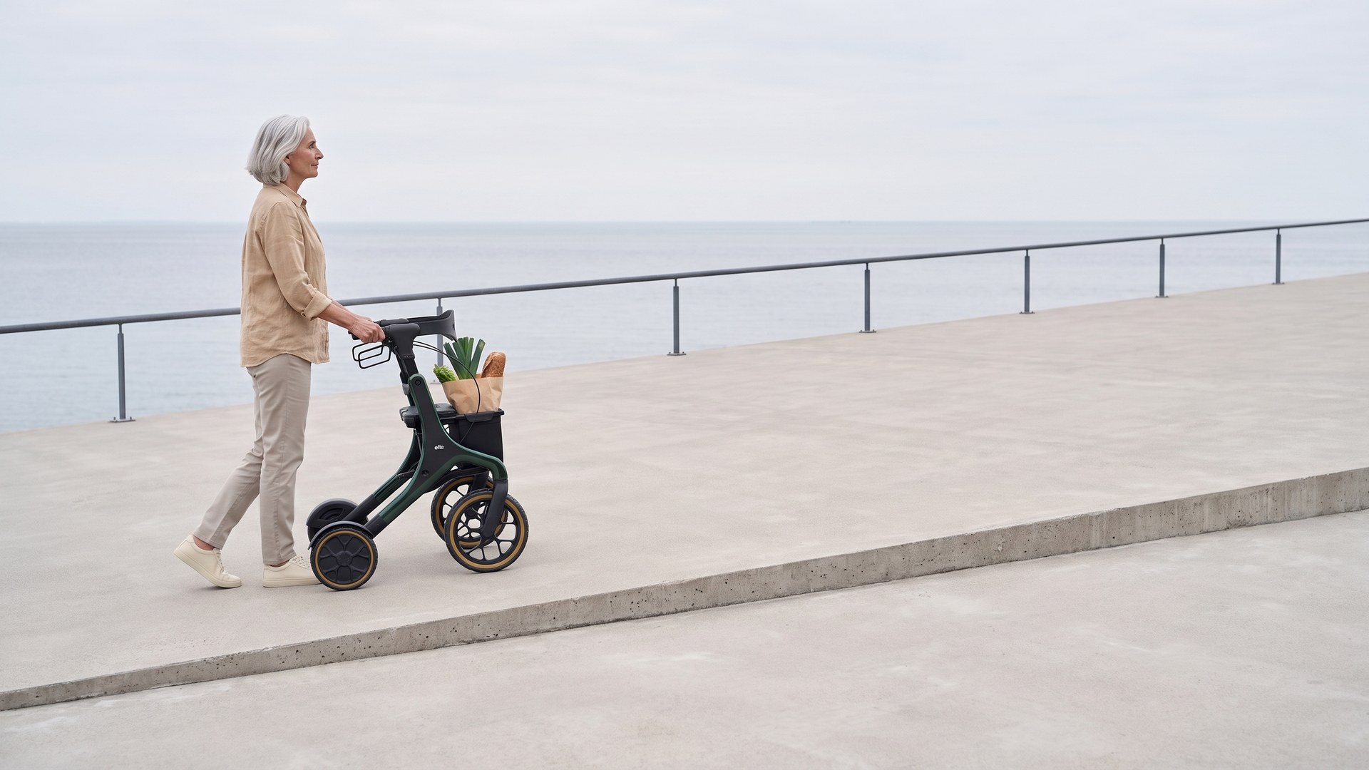 Eine Frau geht mit dem ello an einer Uferpromenade am Meer entlang